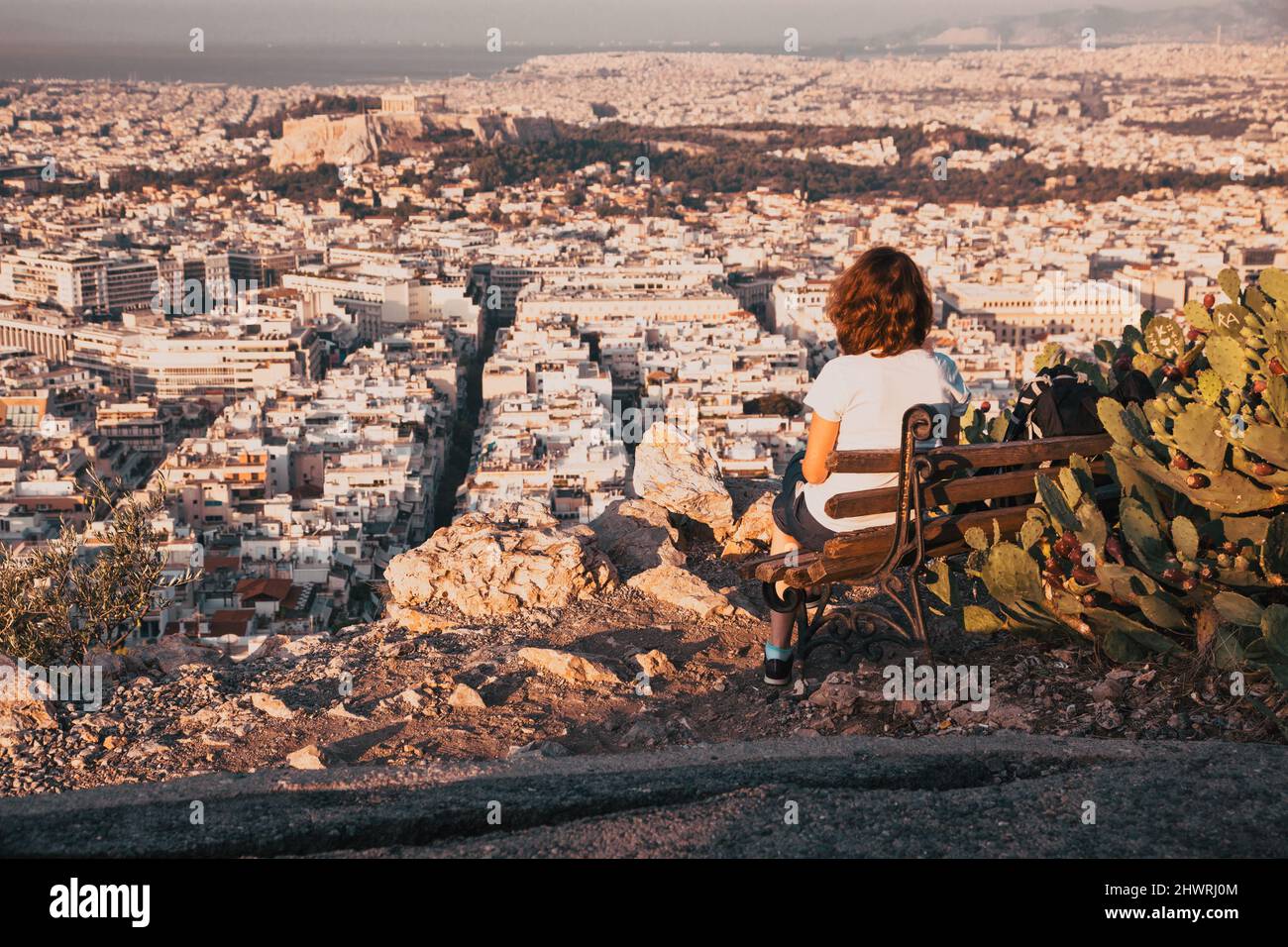 woman sitting on Lycabettus Hill, the highest point in the city overlooking Athens with the Acropolis - world traveller Stock Photo