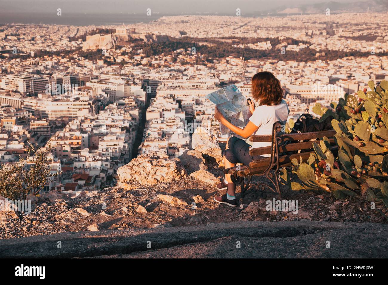 woman with a map sitting on Lycabettus Hill, the highest point in the city overlooking Athens with the Acropolis - world traveller Stock Photo