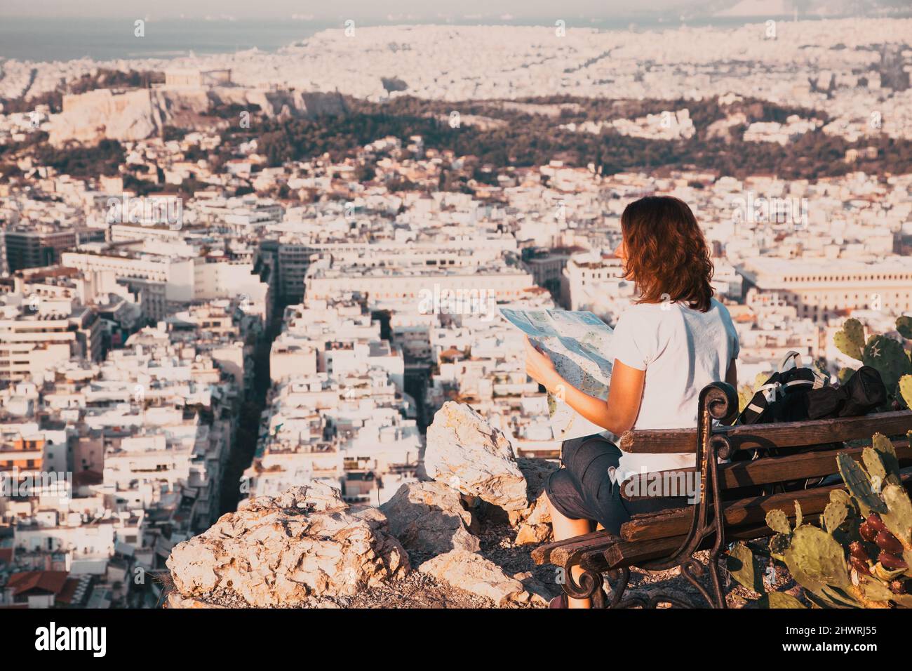 woman with a map sitting on Lycabettus Hill, the highest point in the city overlooking Athens with the Acropolis - world traveller Stock Photo