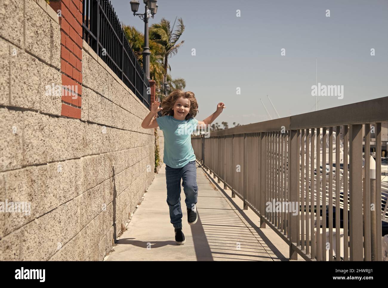 Happy energetic boy child enjoy free time running on promenade during summer vacation, freedom Stock Photo