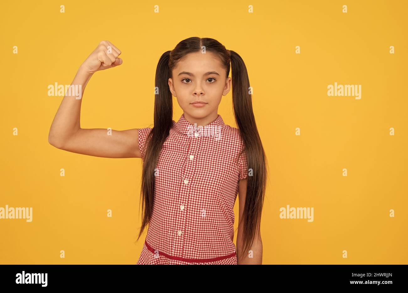 Serious girl child show power gesture flexing arm yellow background, strong Stock Photo