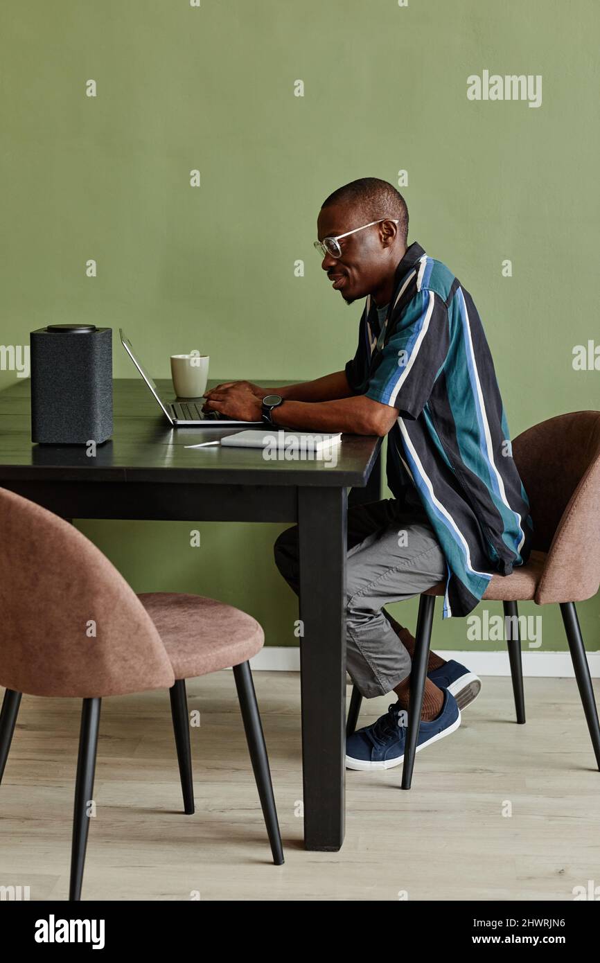 Vertical side view portrait African American man using laptop at home ...