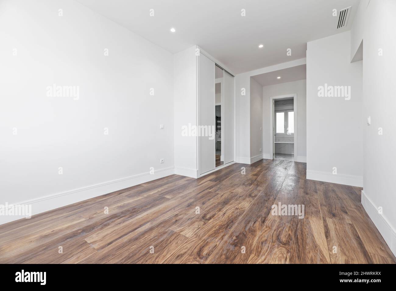 Spacious empty bedroom with dark wooden floorboards, fitted mirrored wardrobes and access to an en-suite toilet Stock Photo