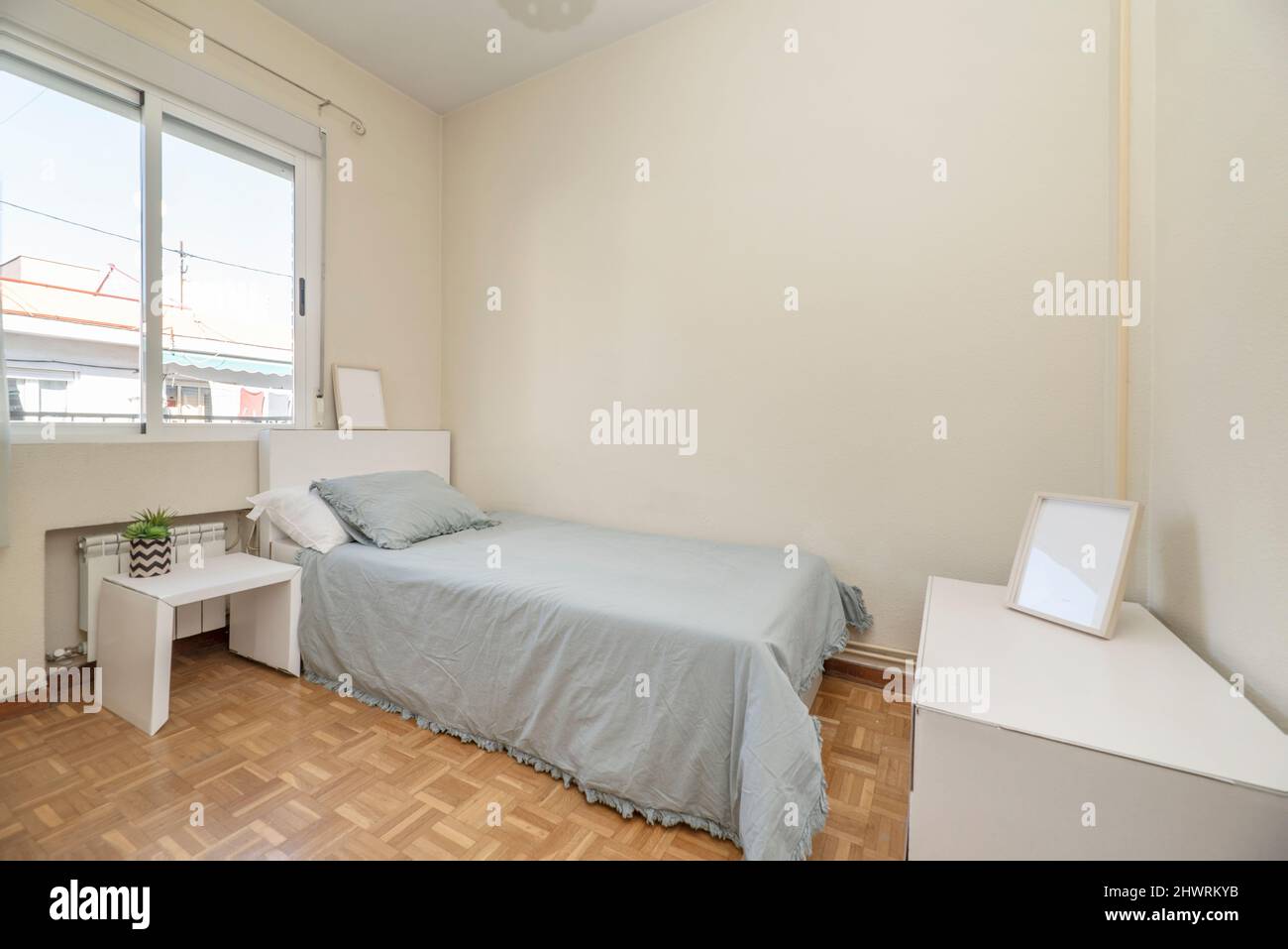 Single bed with blue bedspread with white headboard, matching side