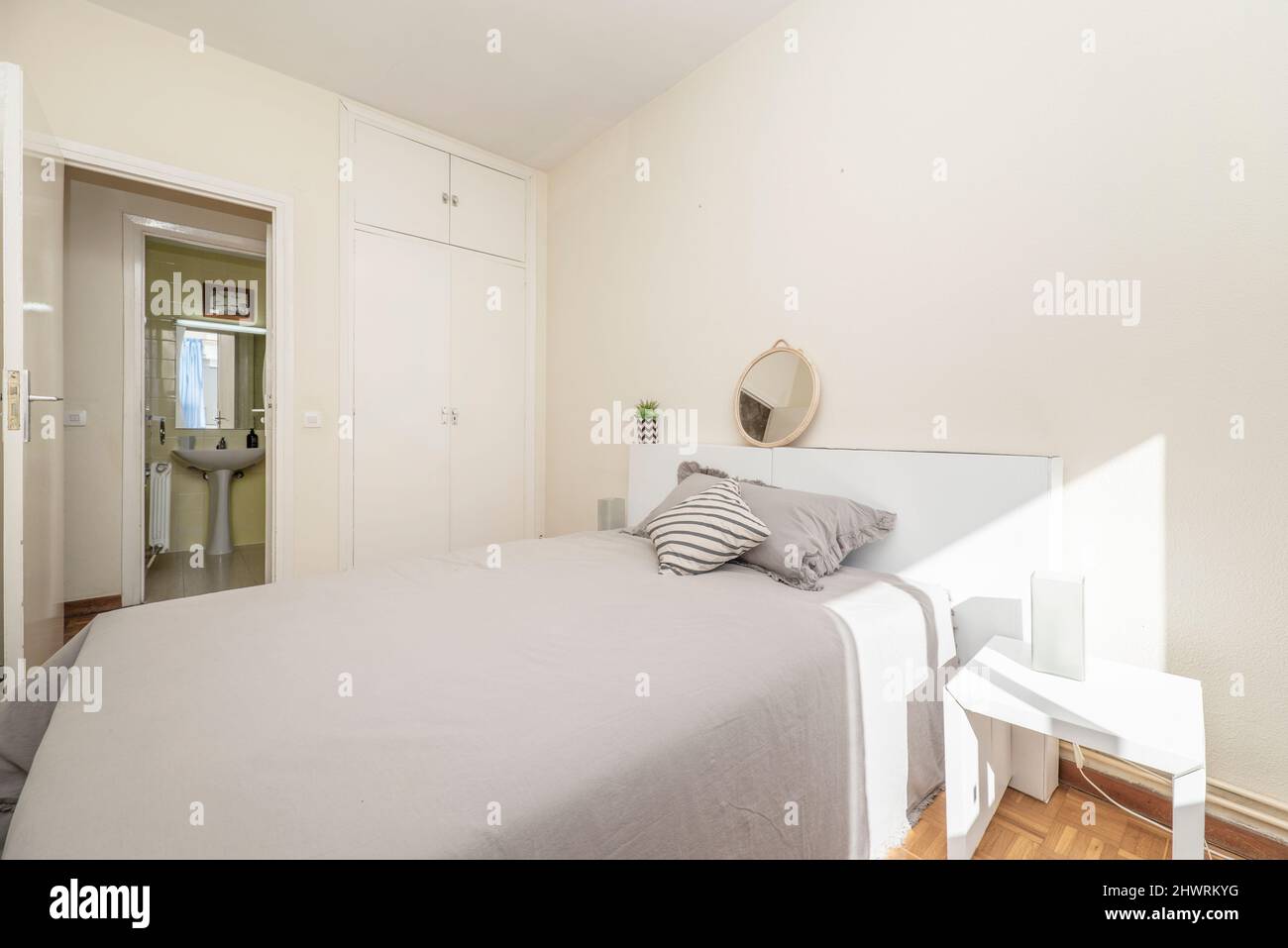 bedroom with king size bed with gray bedspread and cushions, white headboard, white wooden doors built-in wardrobe and en-suite toilet Stock Photo