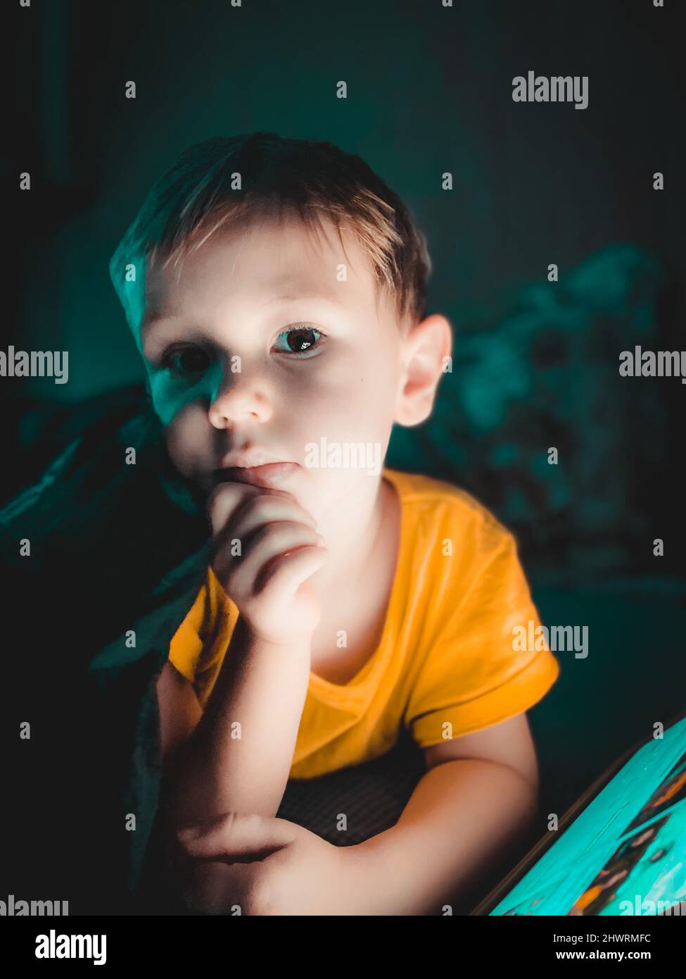 Little caucasian boy looking at a tablet in the evening in the dark on the bed,lifestyle toned photography at home, selective focus and softfocus Stock Photo