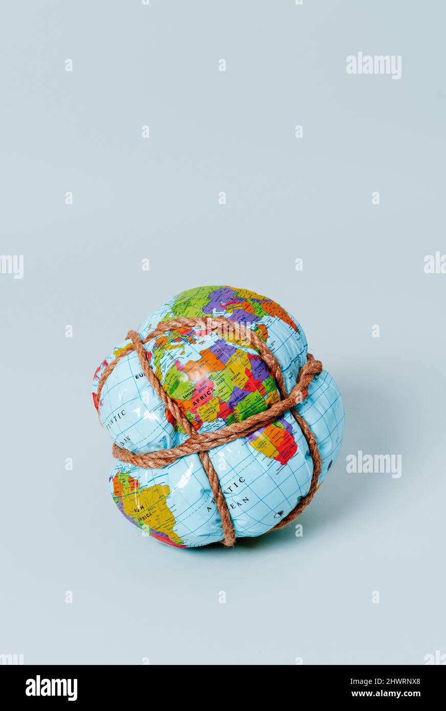 an earth globe tightly tied with rope on a pale blue background, with ...