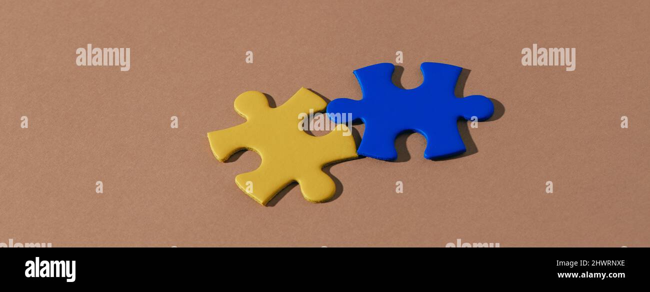 high angle view of two puzzle pieces with the colors of the ukrainian flag on a brown background, in a panoramic format to use as web banner or header Stock Photo