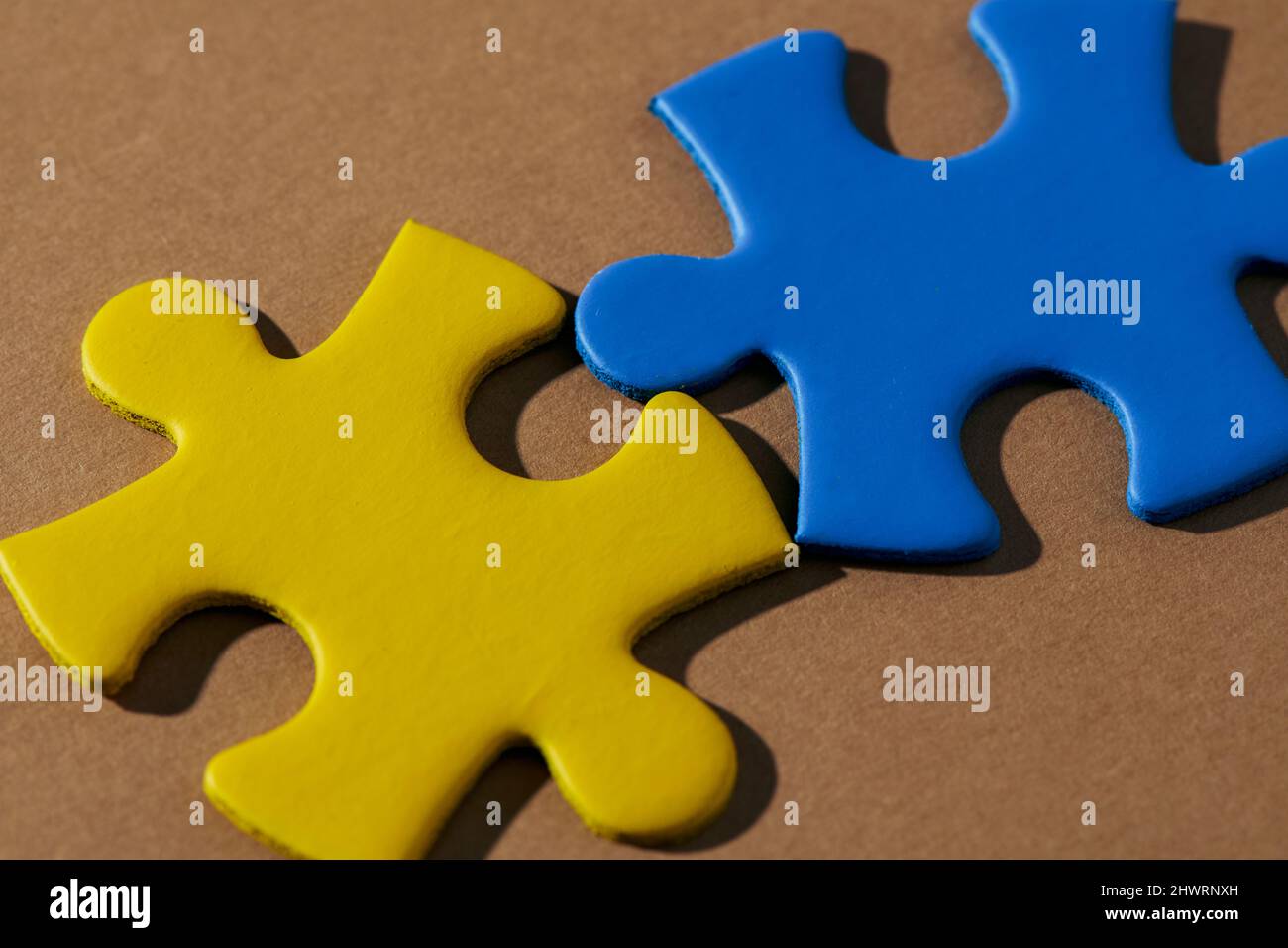 two jigsaw pieces with the colors of the ukrainian flag on a brown background Stock Photo