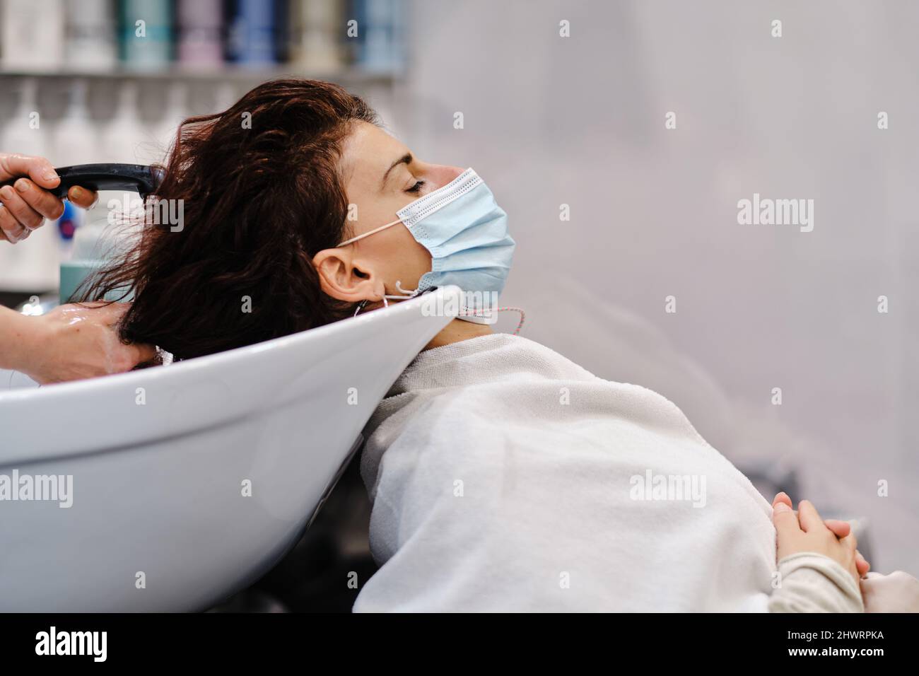 Woman with a face mask relaxing while hairdresser washing her hair at the hair salon. Stock Photo
