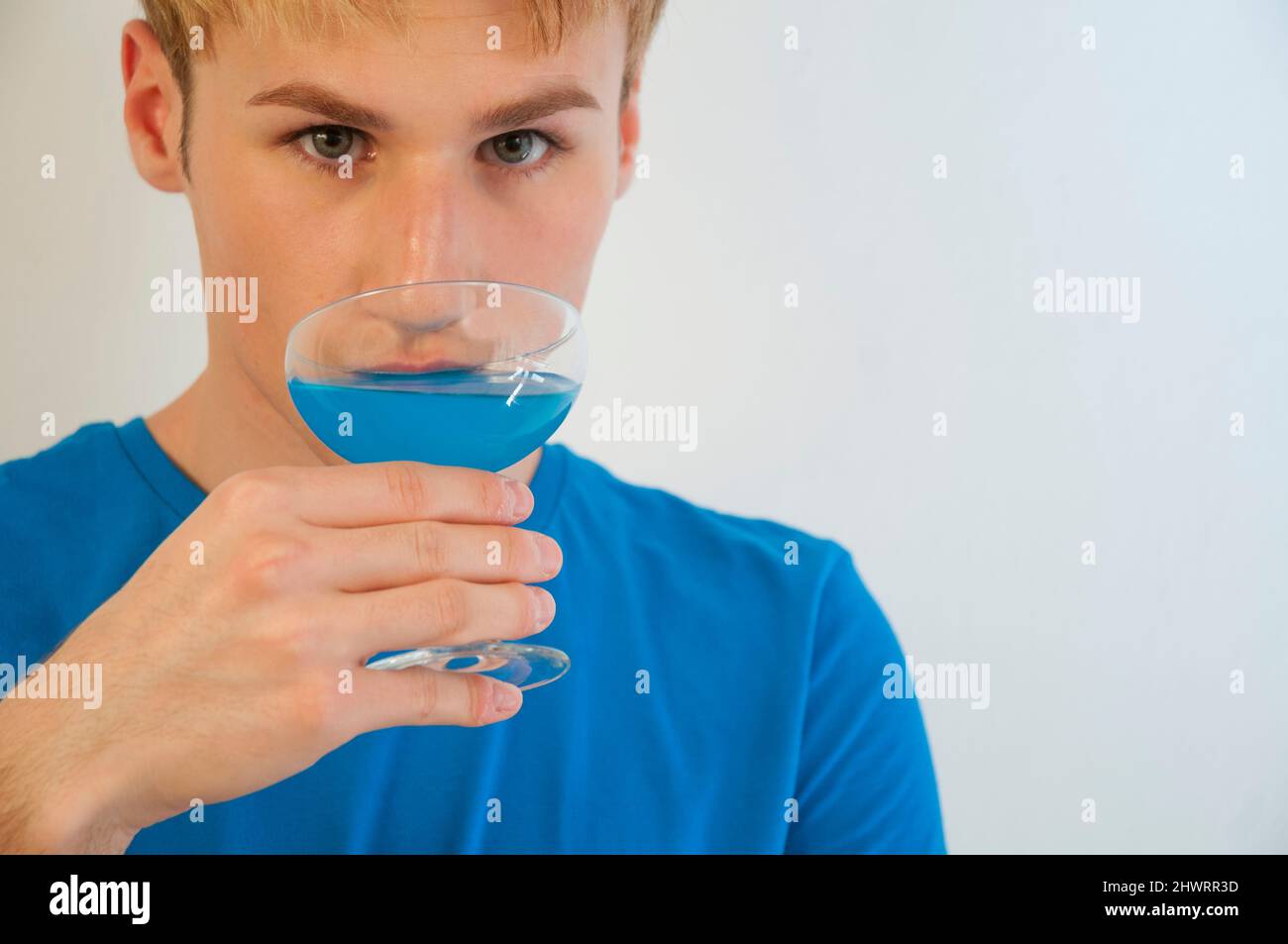 Young man drinking a blue drink and looking at the camera. Close view. Stock Photo