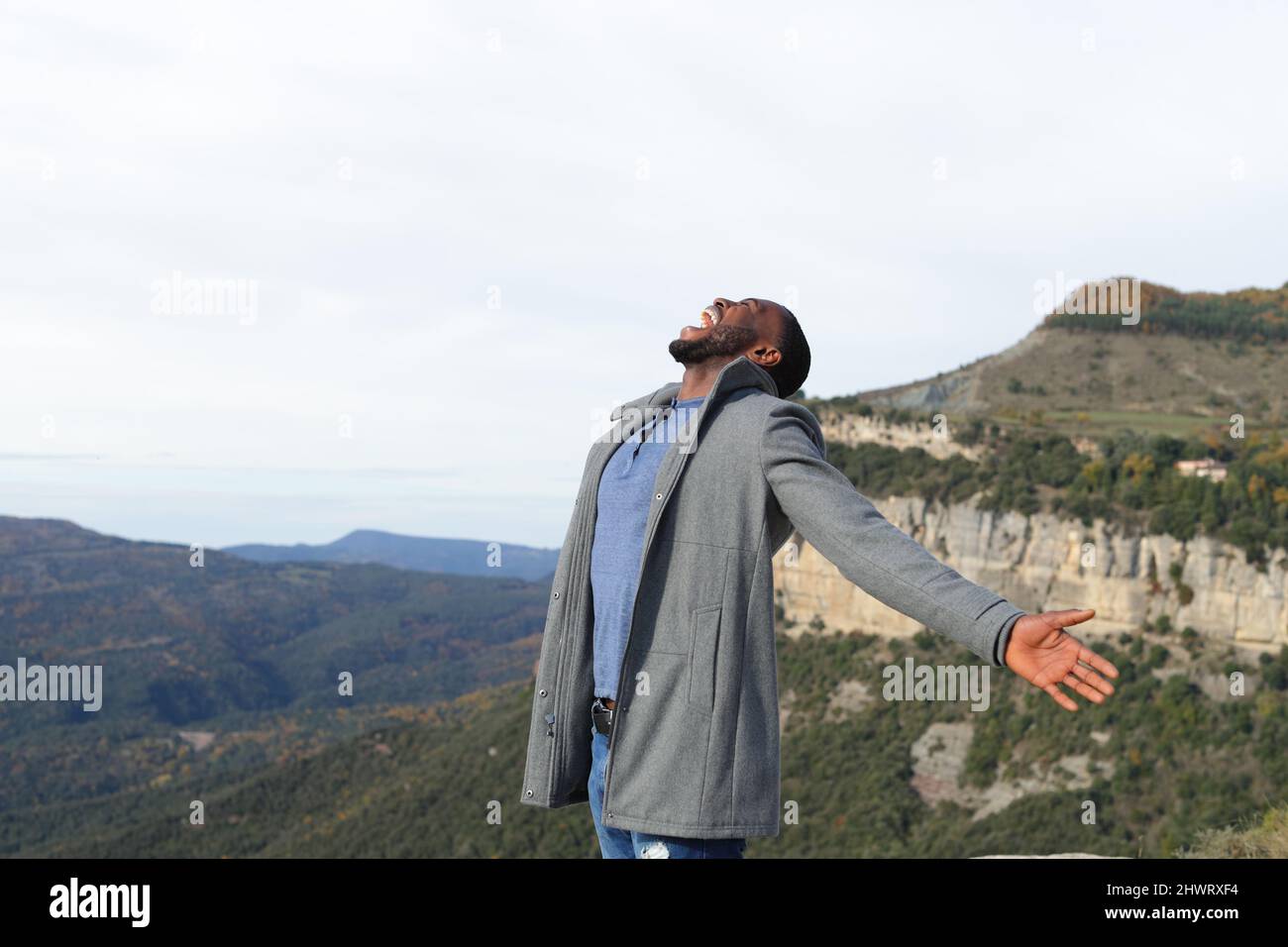 Euphoric man with black skin outstretching arms celebrating in winter in the mountain Stock Photo