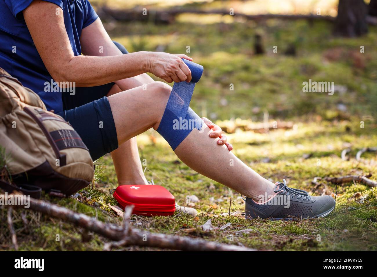 Injured hiker putting elastic bandage to her knee. Injury during hiking