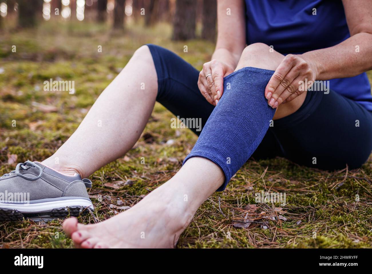 Hiker putting elastic orthopaedic bandage during hiking. Woman feeling pain of joint and knee after injury. First aid of torn ligament or knee sprain Stock Photo