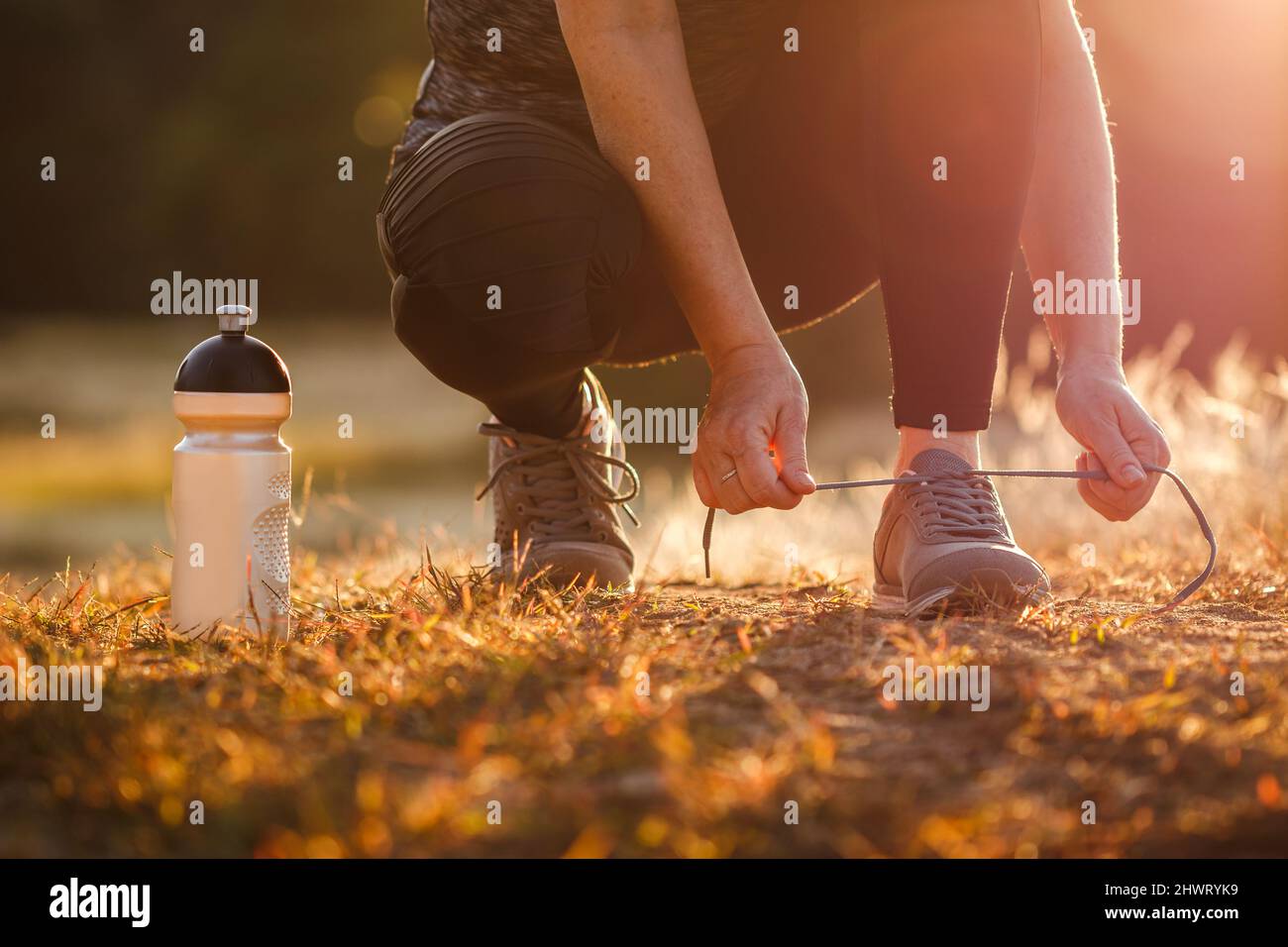 Woman tying shoelace of running shoe. Getting ready for jogging outdoors during sunset. Fitness, running and active lifestyle Stock Photo