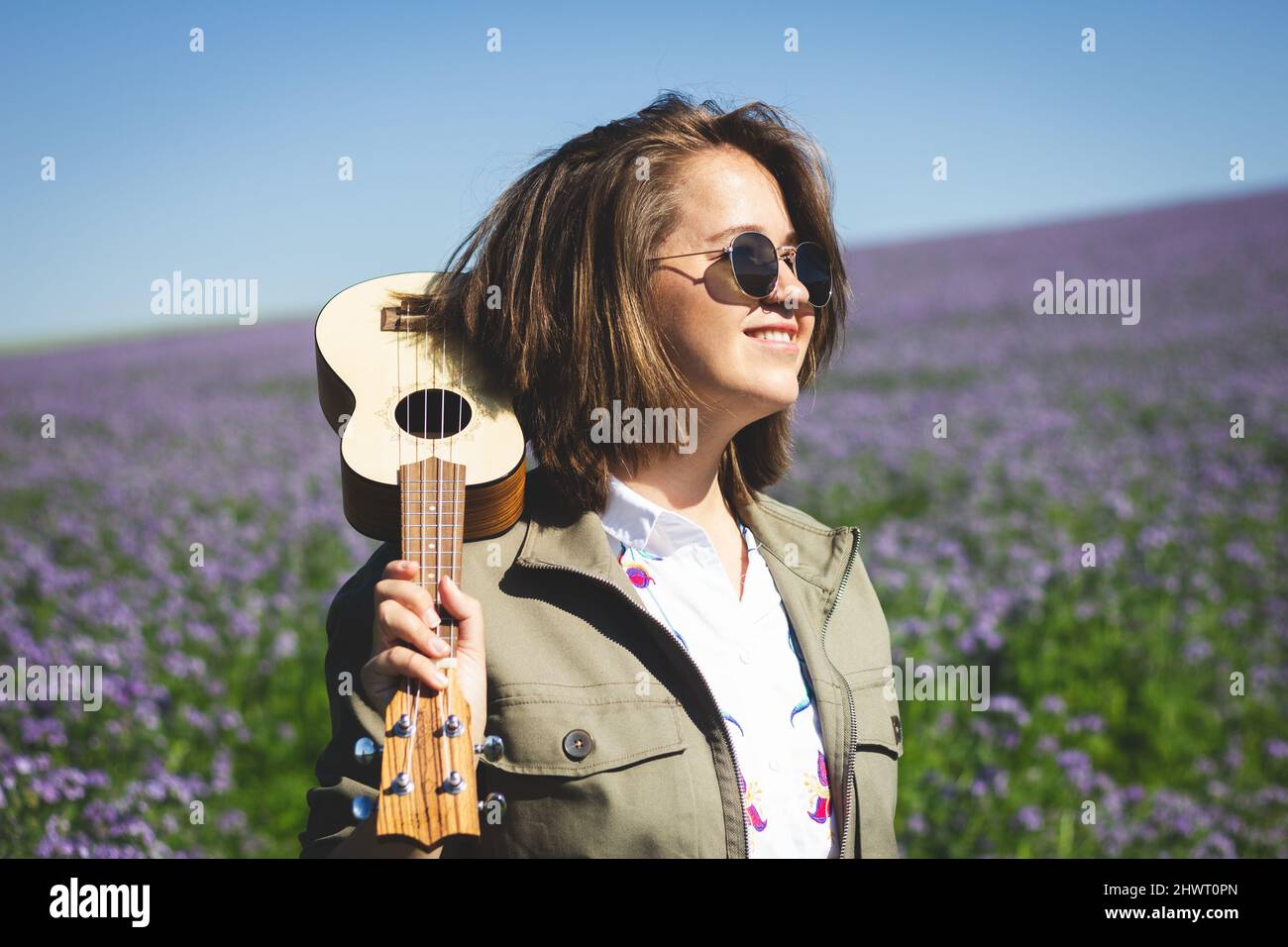 Happy young smiling woman with ukulele enjoying sunlight outdoors at spring Stock Photo