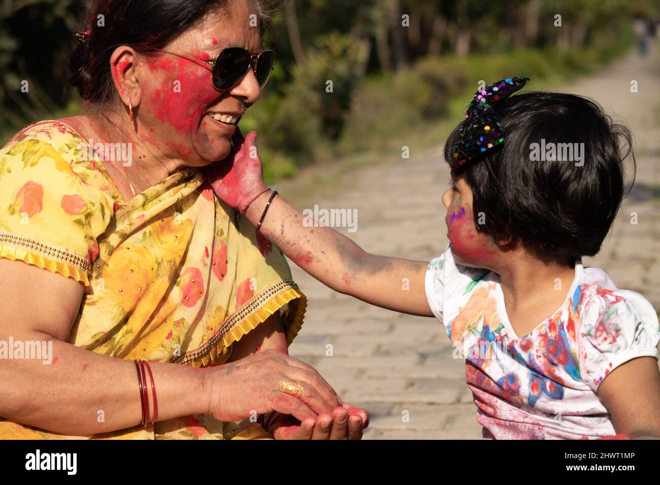 Elderly Indian Lady And Kid Enjoying Holi With Gulal Or Abir Rang Abeer. Festive, Family, Fun, Celebration, Enjoyment, Togetherness, Multi Generation Stock Photo