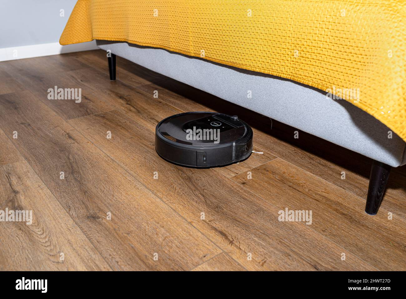 A modern robotic vacuum cleaner cleans the vinyl panels under the bed