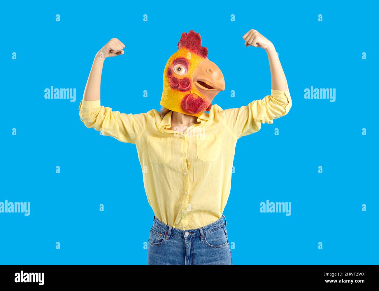 Young woman wearing funny chicken mask pretending to be strong and flexing her arms Stock Photo