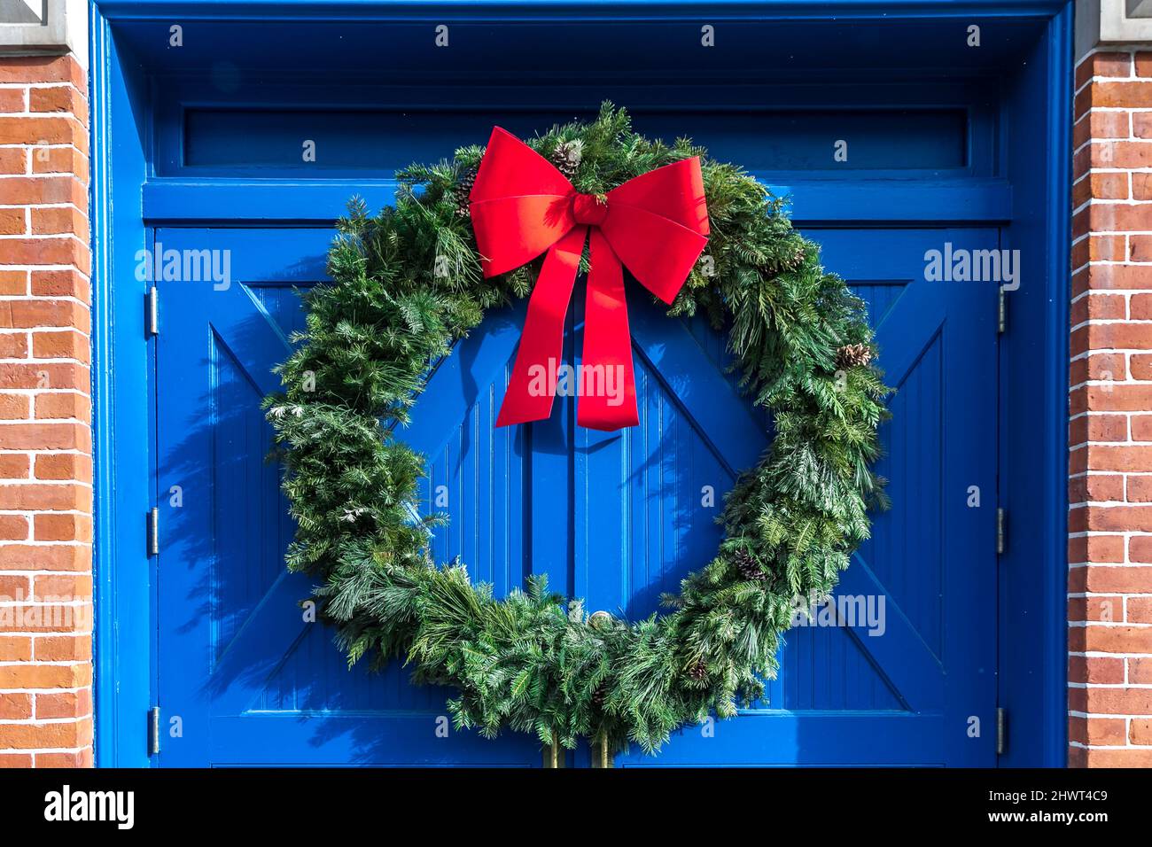A large green outdoor Christmas holiday wreath with a bright red bow against a pair of bright cobalt blue doors Stock Photo