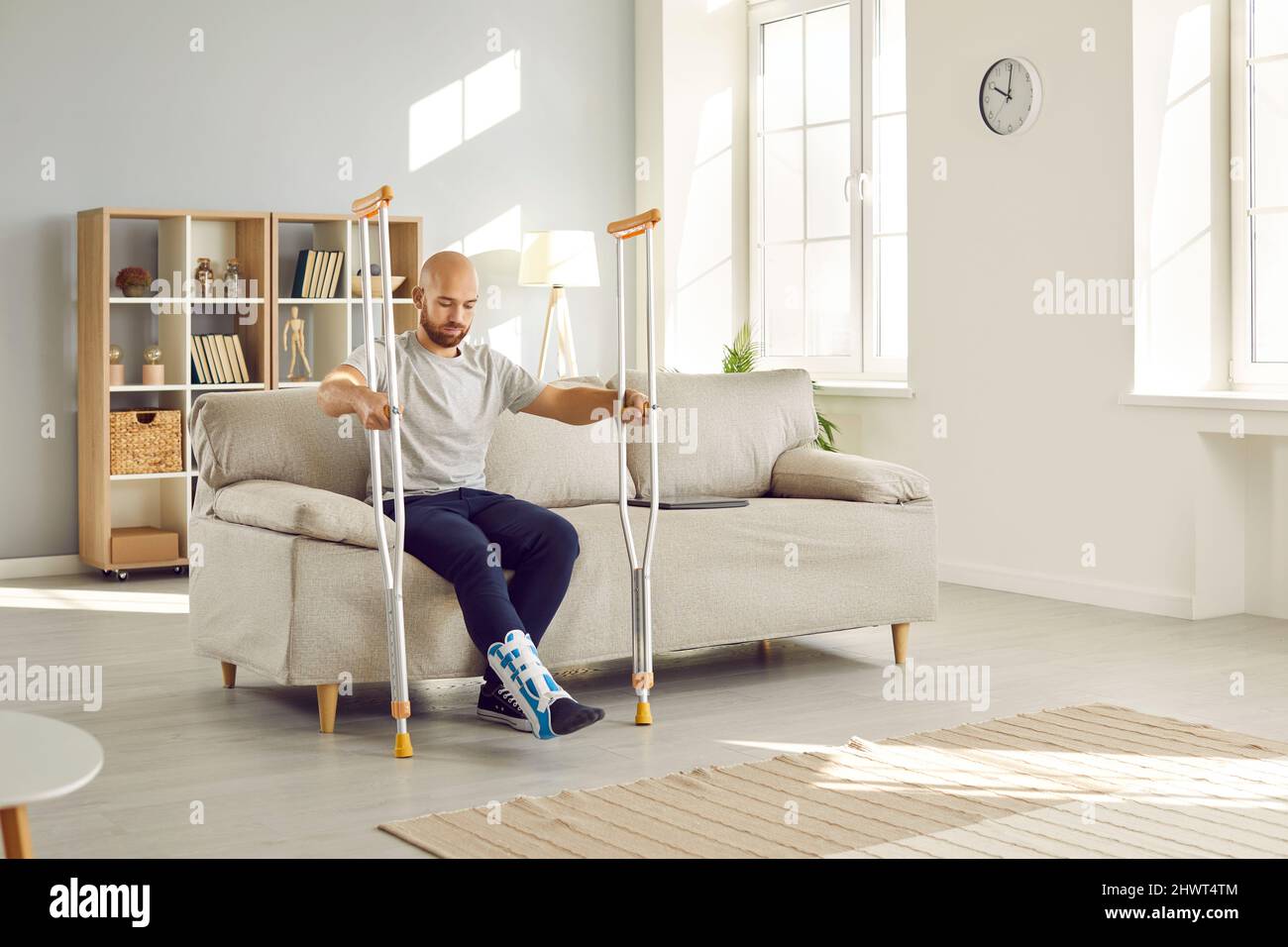 Young man with leg injury leans on crutches while trying to get up from