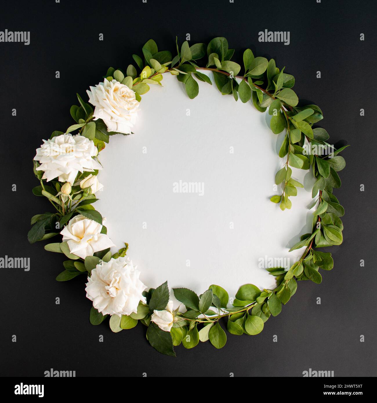 Round frame wreath with white roses bloom and branches on black