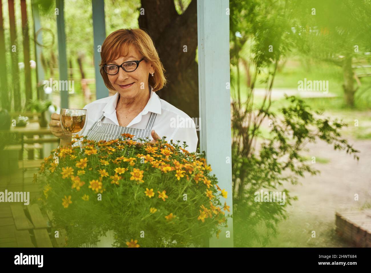 Happy aged woman enjoying tea on blooming terrace Stock Photo