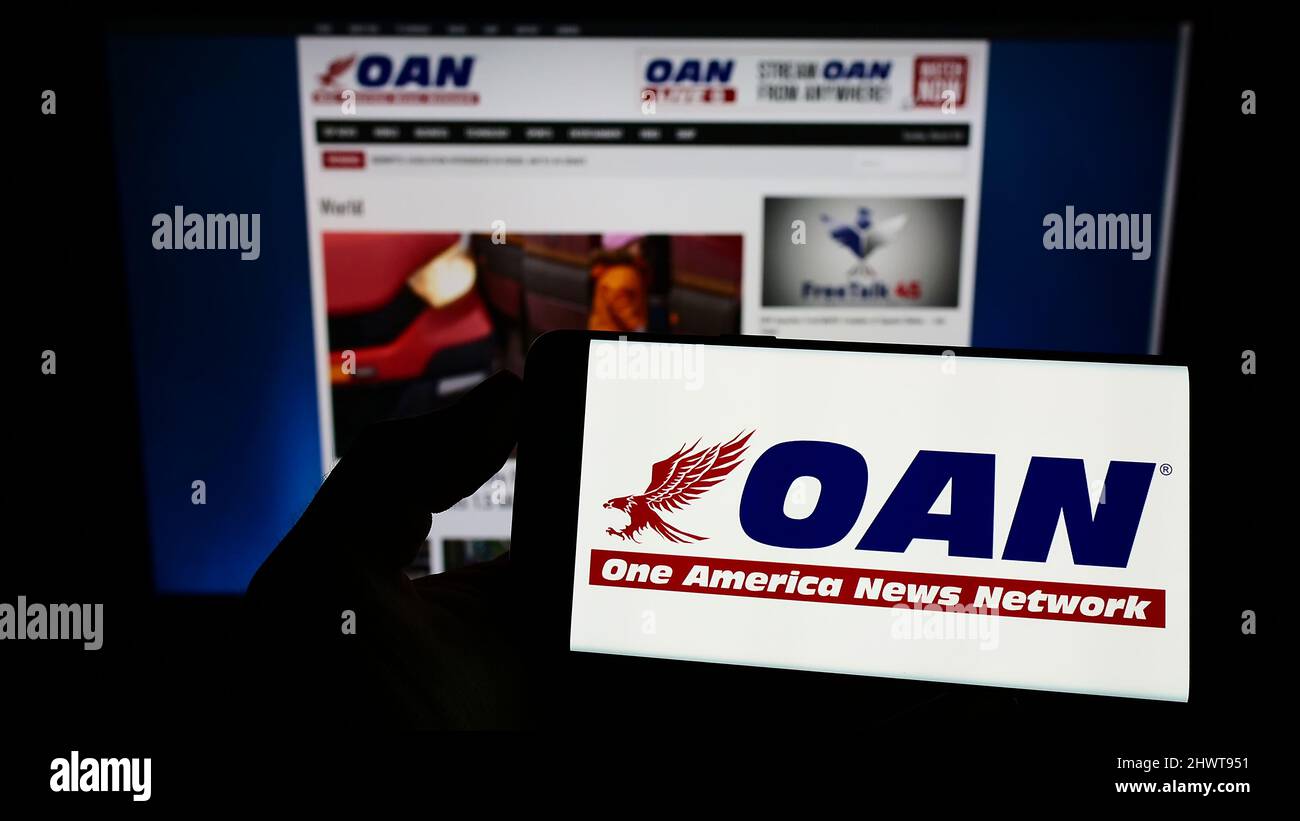 Person holding mobile phone with logo of US media company One America ...