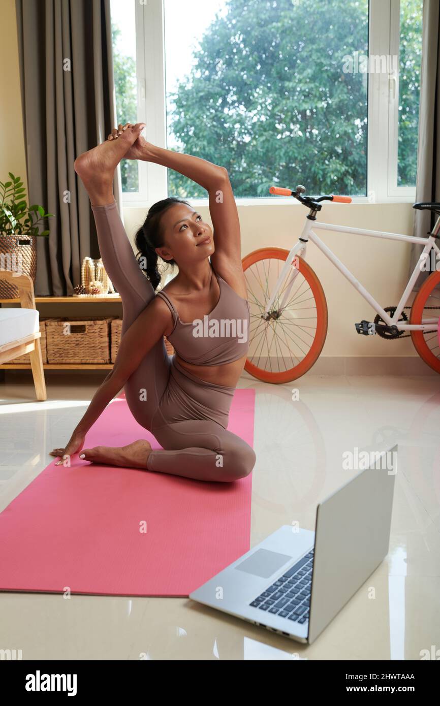 Fit woman doing yoga exercise while watching tutorial on laptop at