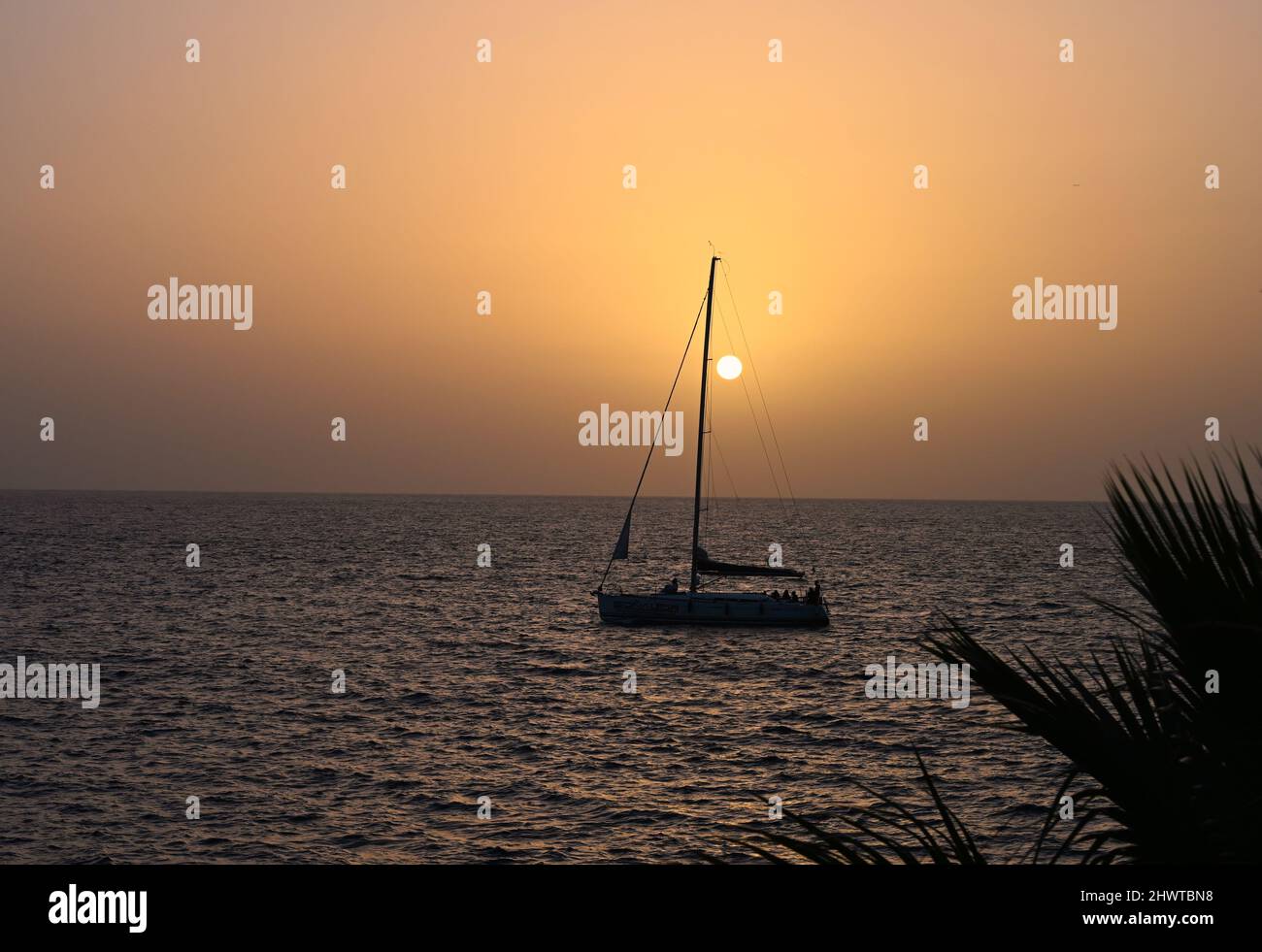A tranquil distant sunset on a warm February Day over the Atlantic Ocean at dusk with a sail boat crossing the horizon Stock Photo