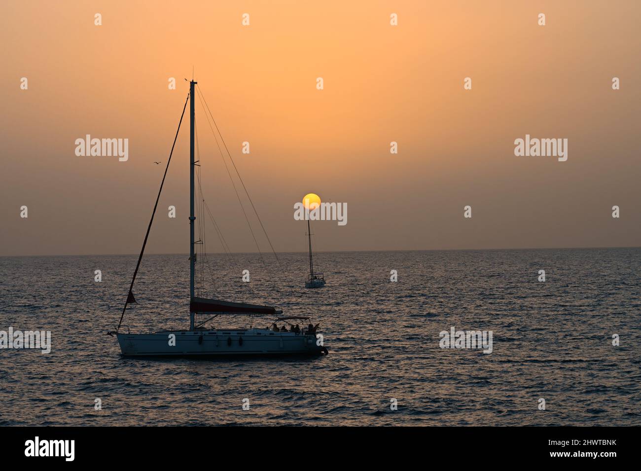 A tranquil distant sunset on a warm February Day over the Atlantic Ocean at dusk with two sail boat crossing the horizon Stock Photo