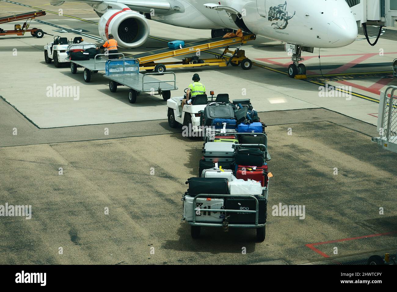 Baggage Handler loading and unloading baggage onto commercial airliner on a busy airport Stock Photo