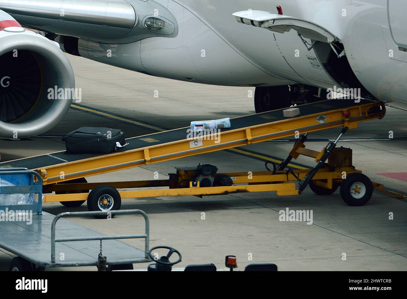 Baggage Handler loading and unloading baggage onto commercial airliner on a busy airport Stock Photo
