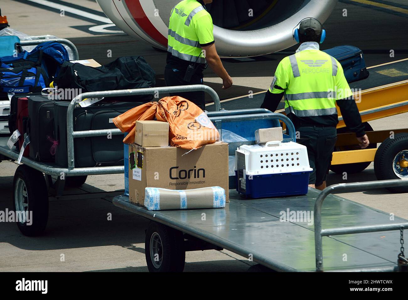 Baggage Handler loading and unloading baggage onto commercial airliner on a busy airport Stock Photo