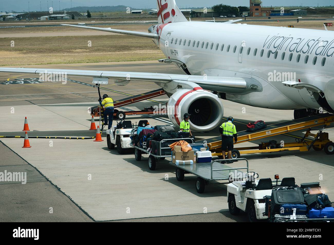 Baggage Handler loading and unloading baggage onto commercial airliner on a busy airport Stock Photo