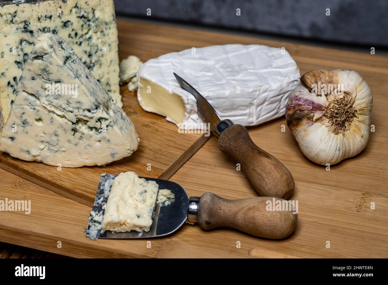 assorted cheese board with special knives for cutting cheese and a head of garlic in one corner Stock Photo