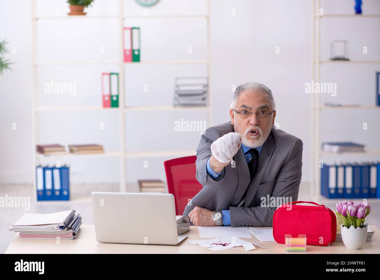 Old businessman employee cutting his hand at workplace Stock Photo