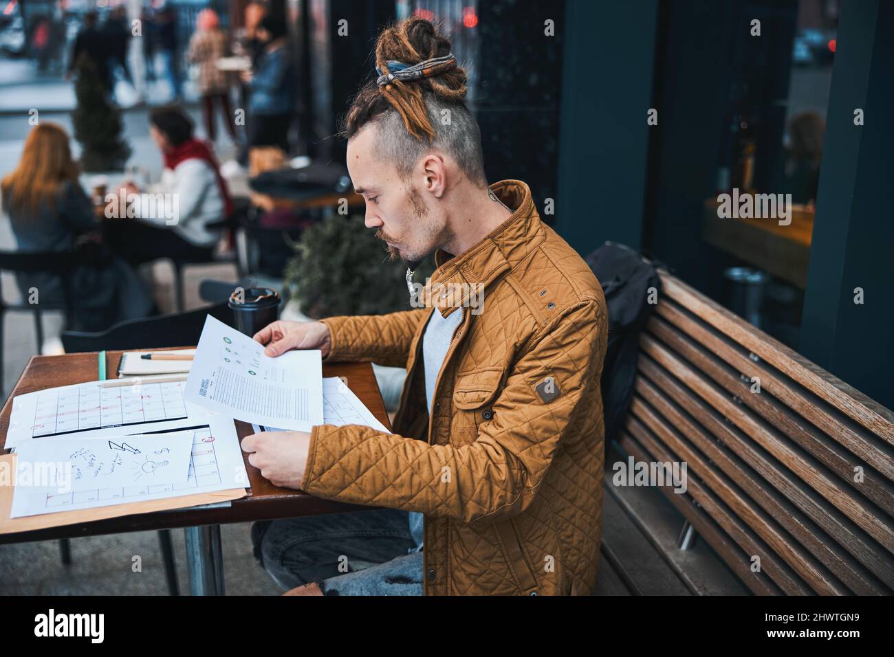 Young man with papers drinking coffee outdoors Stock Photo