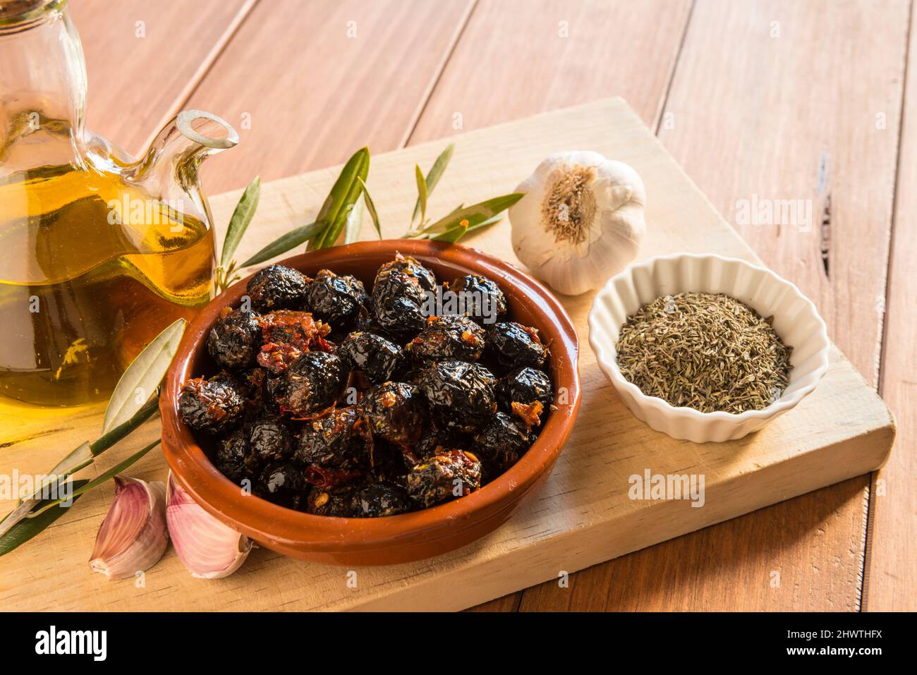 Still life with a bowl of olives, together with different seasonings used for their dressing, on a wooden board. Homemade preparation of olives, tradi Stock Photo