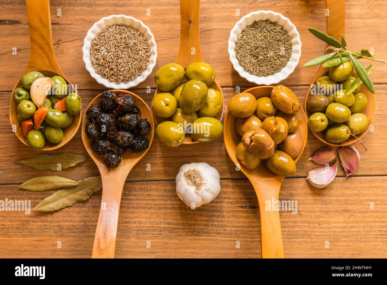 Still life with different varieties of olives, presented in wooden ladles, seasoned with different traditional dressings. Traditional homemade dressin Stock Photo