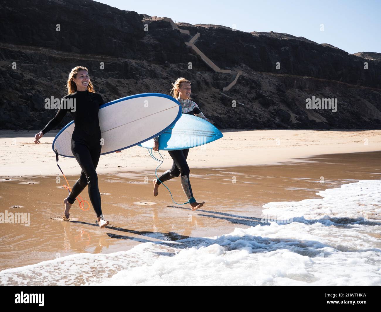 2 Female surfers on the beach running to the water Stock Photo