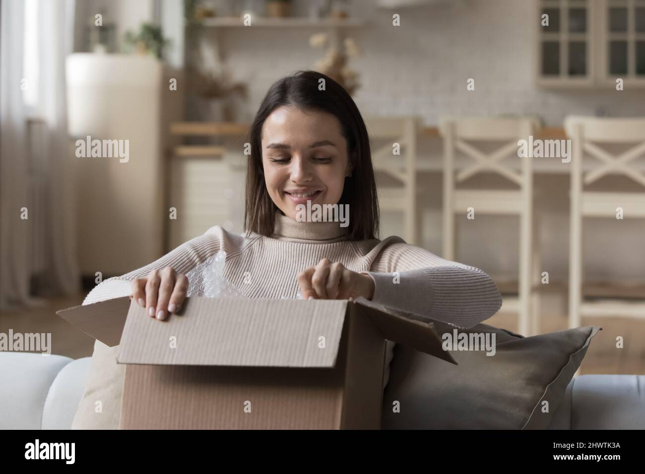 Attractive woman sit on sofa opens parcel box feels happy Stock Photo