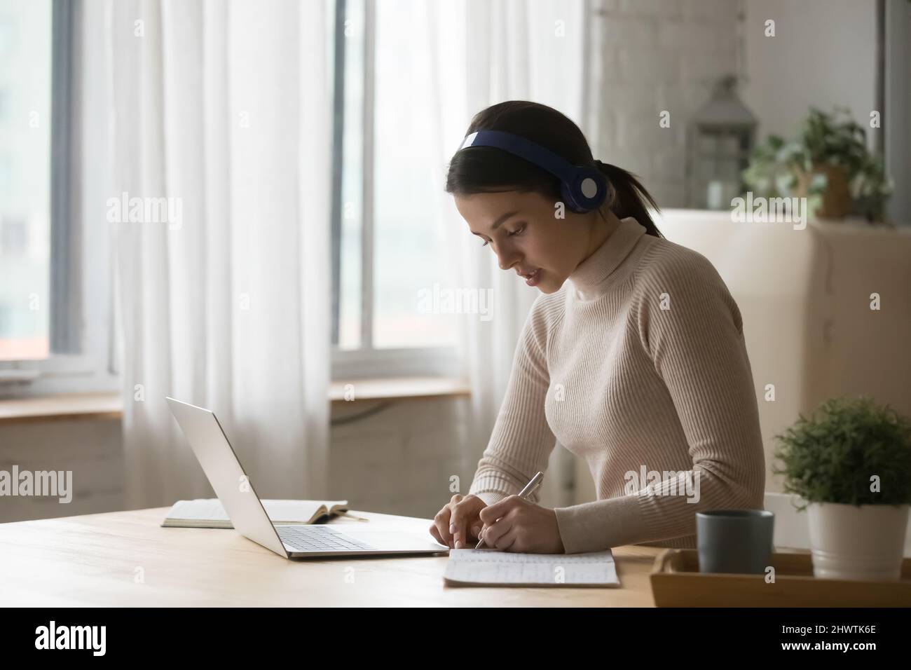 Woman wear headphones listens audio course, jotting in copybook Stock Photo