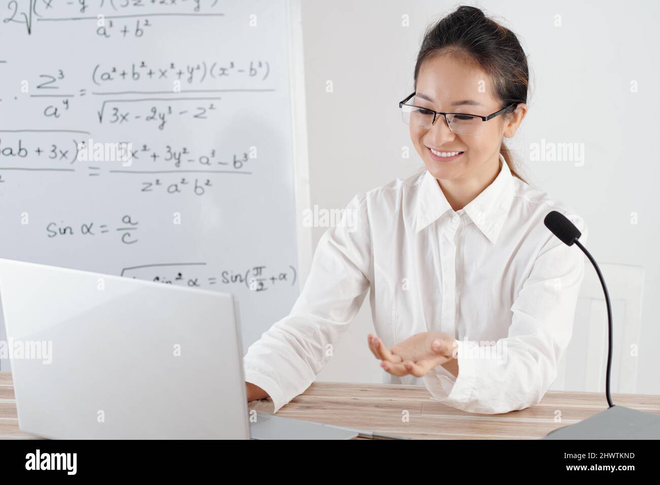Smiling young woman teaching remotely from home, whiteboard with math