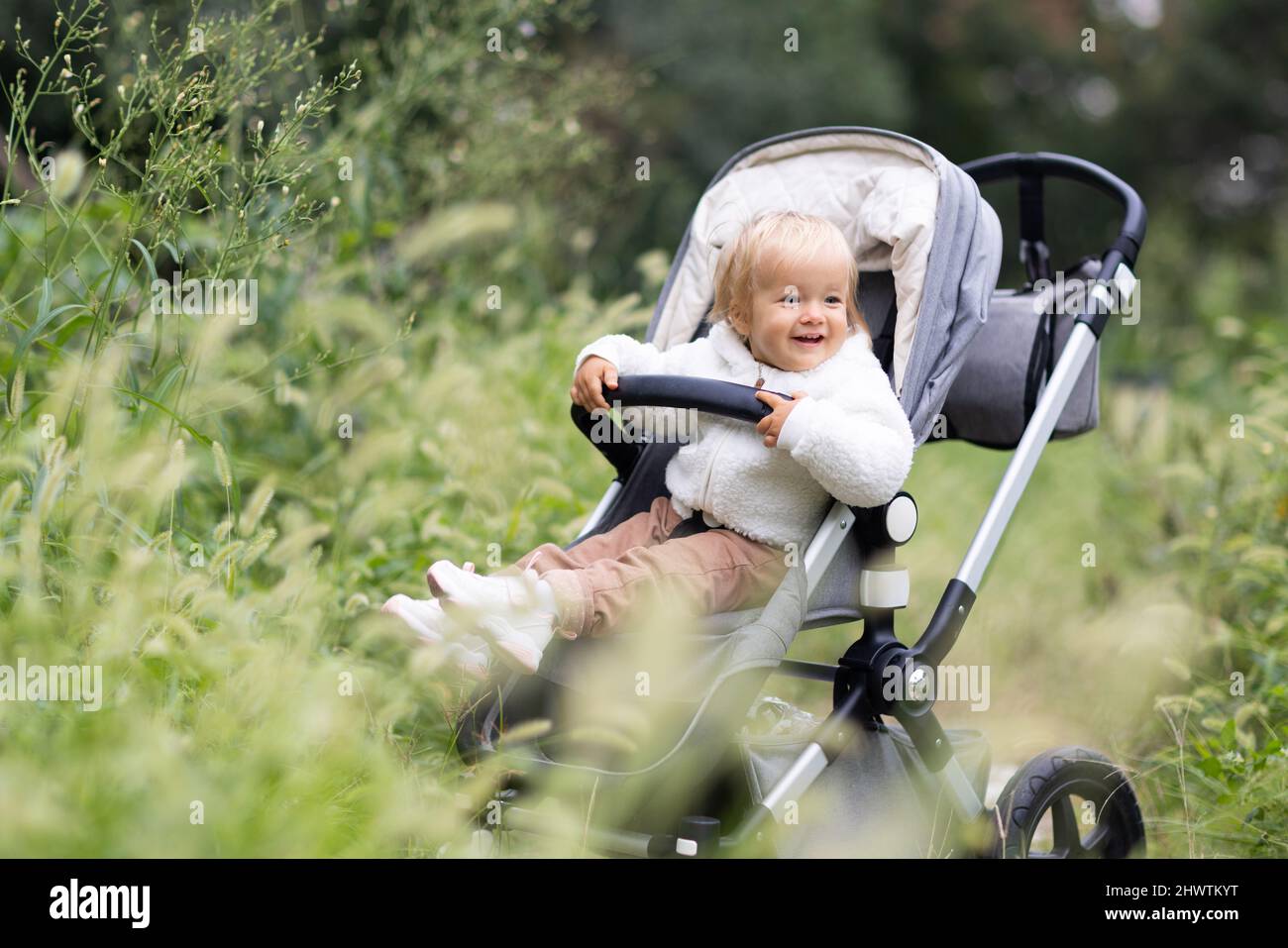 Sweet caucasian baby girl one year old sitting in stroller outdoors at autumn. Little child in pram. Infant kid sits in pushchair. Autumnal walks with Stock Photo Alamy