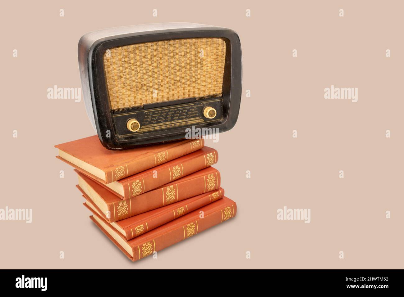 Vintage tube radio1950s 20th century on old books with golden decorations, isolated on light brown background, copy space Stock Photo