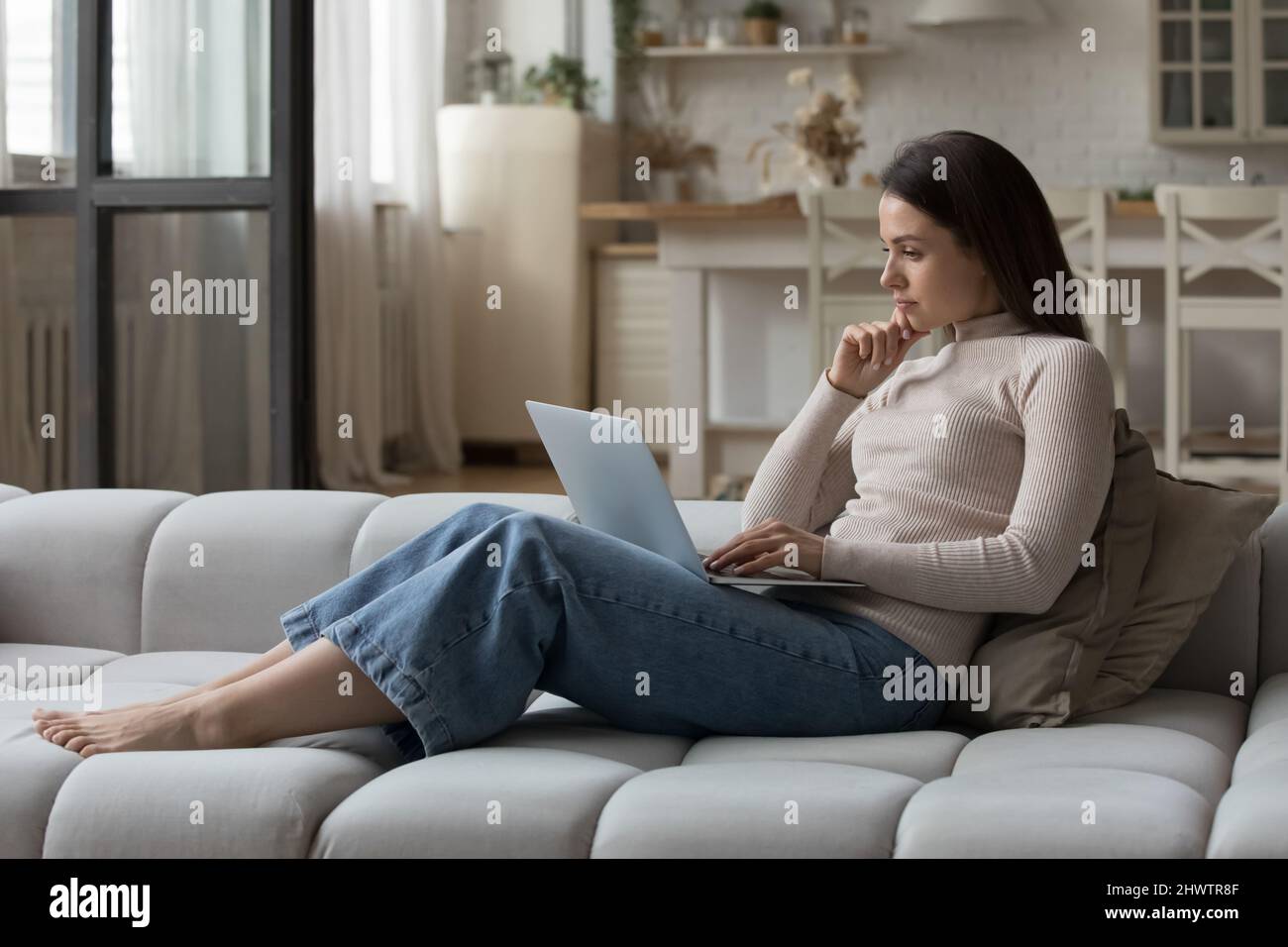 Pensive young woman staring at laptop, feels concerned, looking thoughtful Stock Photo