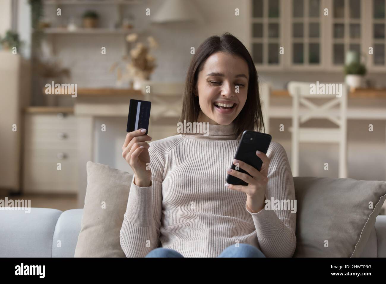 Happy young woman holds smartphone and credit card buying online Stock Photo