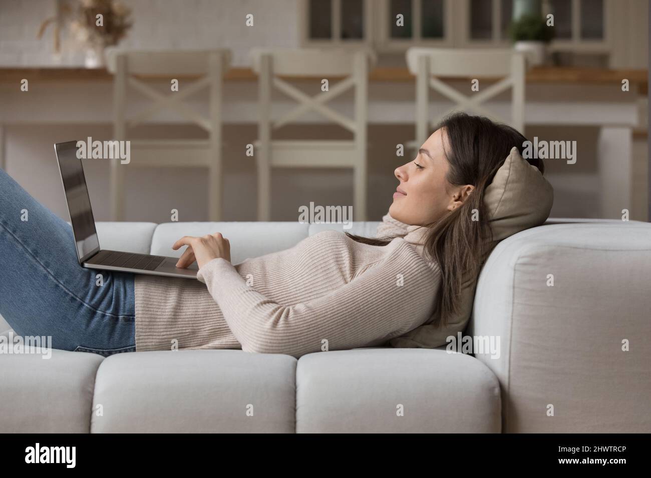 Relaxed young woman lying on cozy sofa with laptop Stock Photo