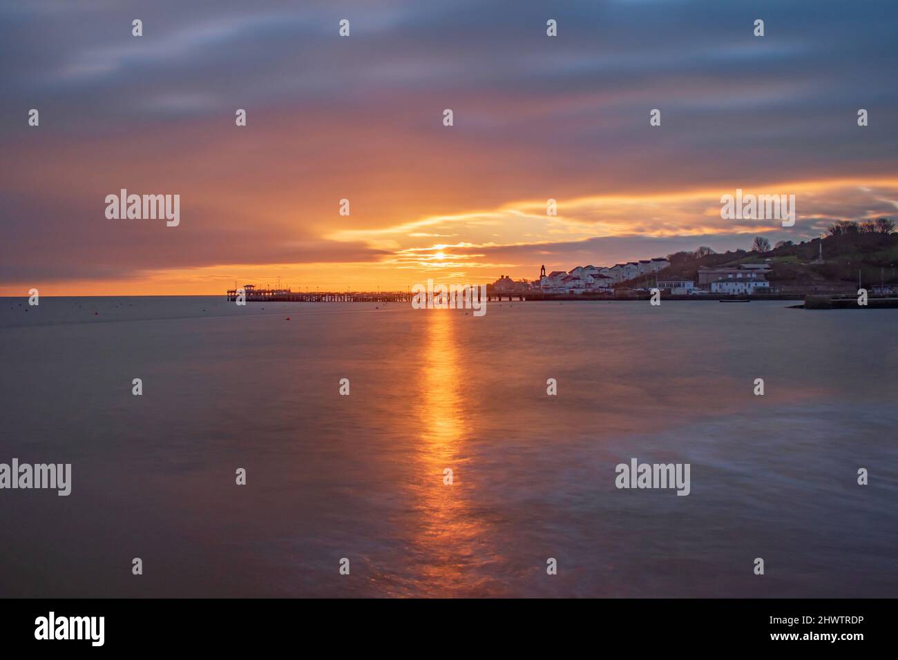 A beautiful glowing sunrise bursts over the smooth sea at the old swanage pier Stock Photo